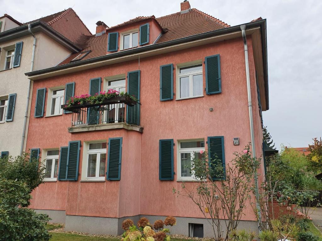 ein rosafarbenes Gebäude mit grünen Rollläden und einem Balkon in der Unterkunft Ferienwohnung Böttger in Dresden