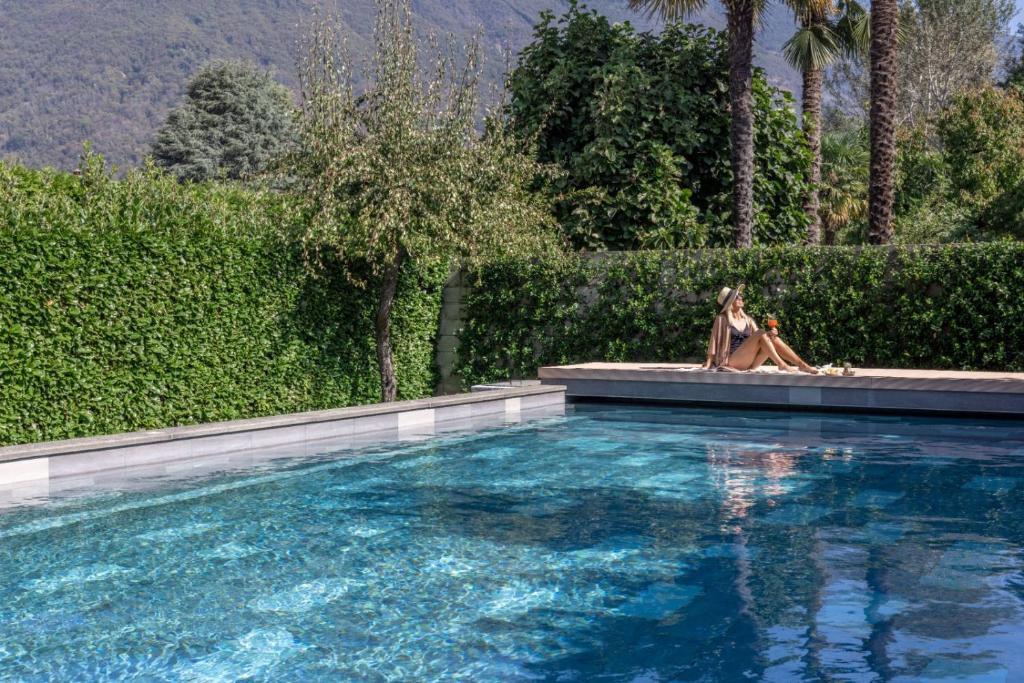 a woman and a dog sitting next to a swimming pool at Ascona Lodge, Pool & Garden Retreat in Ascona