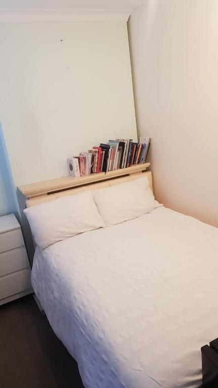 a bedroom with a white bed with a shelf with books at Double bedroom in Raynes Park in London