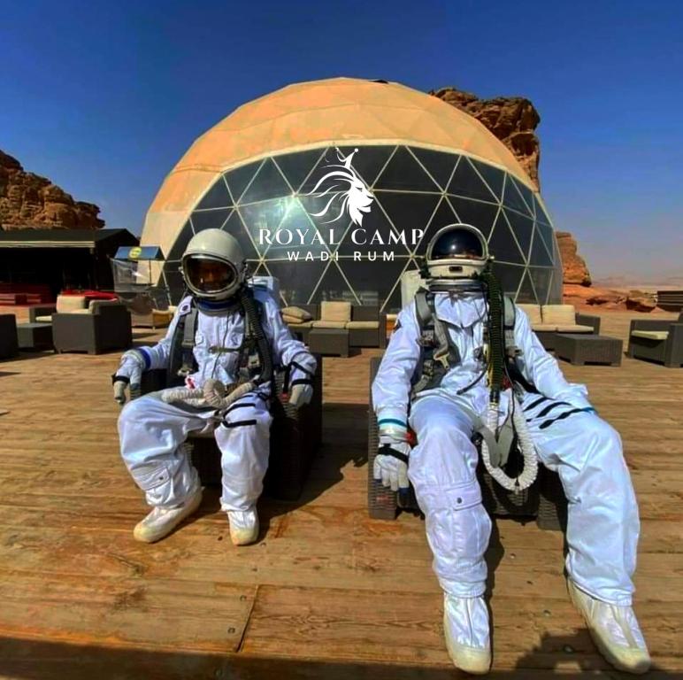 dos personas en trajes espaciales sentados frente a un edificio en ROYAl WADI RUM CAMP, en Wadi Rum