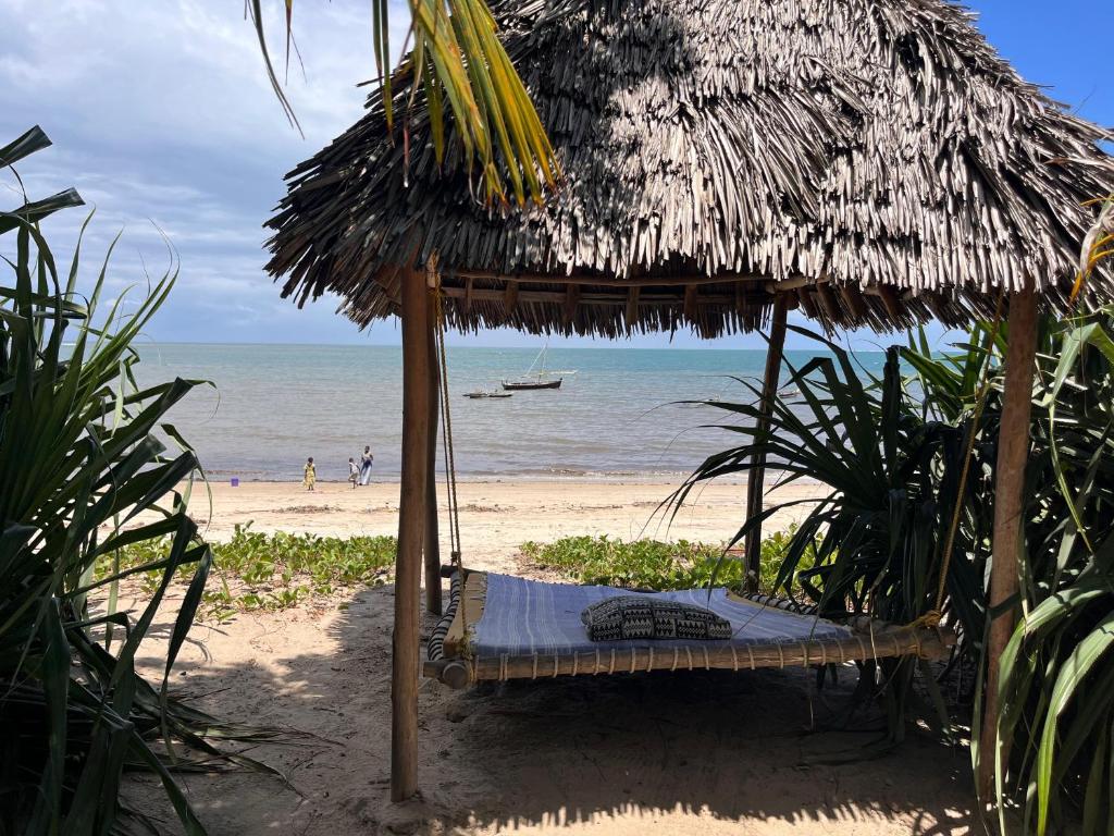 Una cama bajo una sombrilla de paja en una playa en Ushongo Beach Bandas, en Pangani