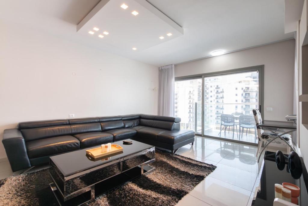 ein Wohnzimmer mit einem Ledersofa und einem Tisch in der Unterkunft O&O Group - Luxury Tower/parking/Shopping Mall/2BR in Qiryat Ono