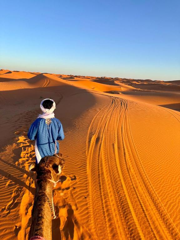 a man standing on a camel in the desert at Fantastic Luxury Dunes Camp in Merzouga