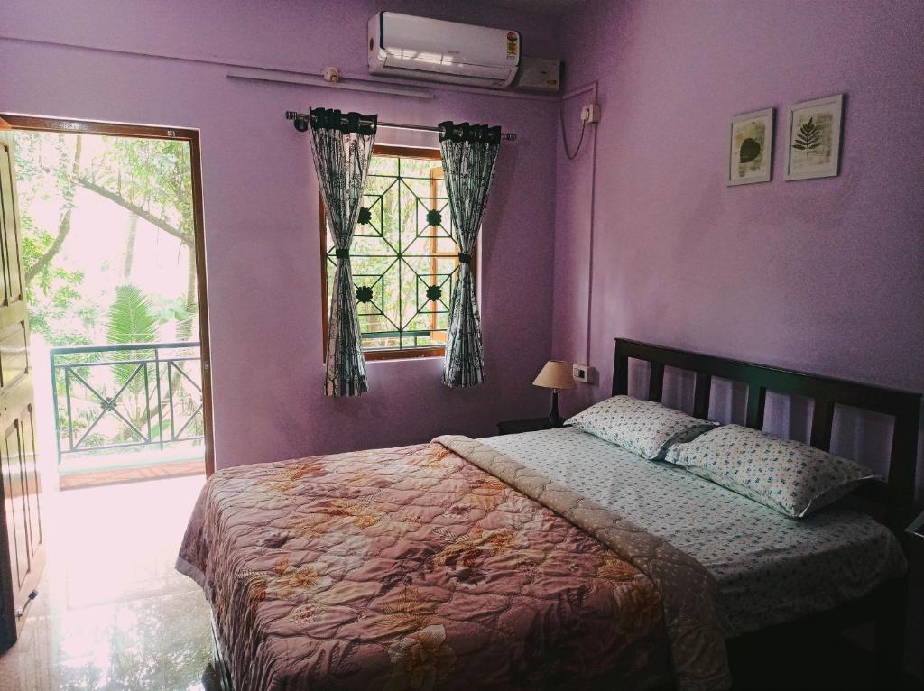 a bedroom with purple walls and a bed with a window at Benirosa Home Stay Apartment 4 in Cansaulim