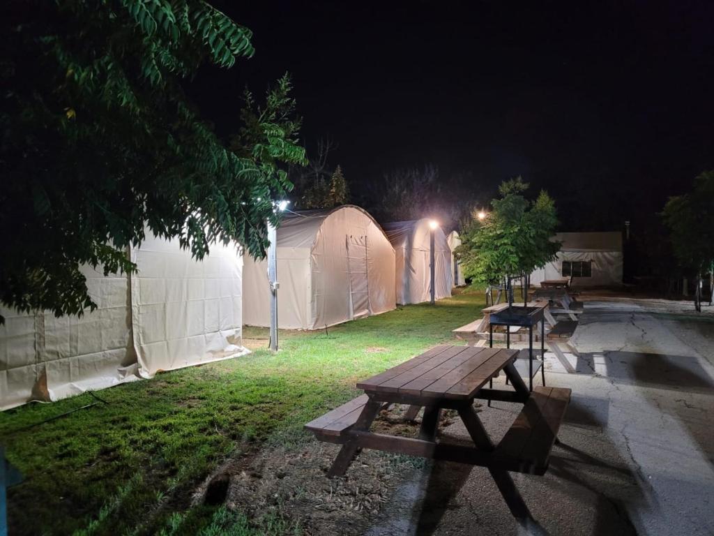 una mesa de picnic frente a algunas tiendas de campaña por la noche en חאן דרך העץ - אוהל ממוזג וקמפינג, en Shadmot Devora