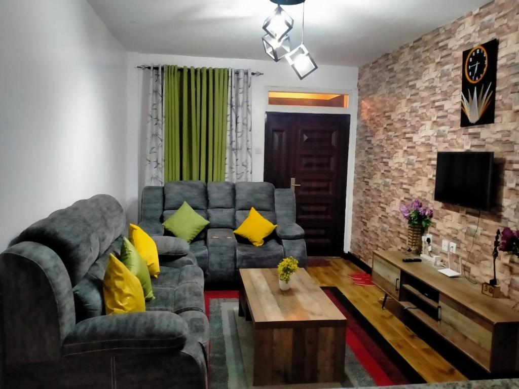 a living room with a gray couch and yellow pillows at One Bedroom Furnished Apartment, Nakuru in Dowsonville