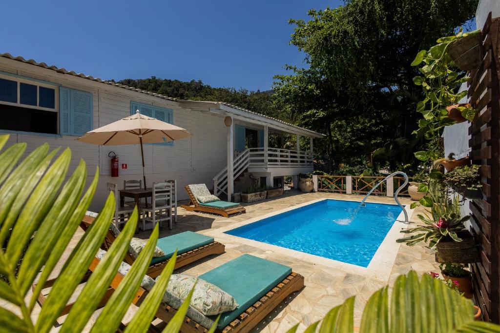 uma piscina com cadeiras e um guarda-sol ao lado de uma casa em Ilhabela Studios em Ilhabela