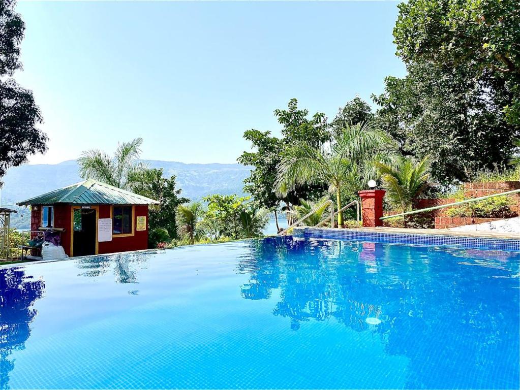 a large blue swimming pool in front of a house at Shivsagar Agro Tourism, Tapola in Mahabaleshwar