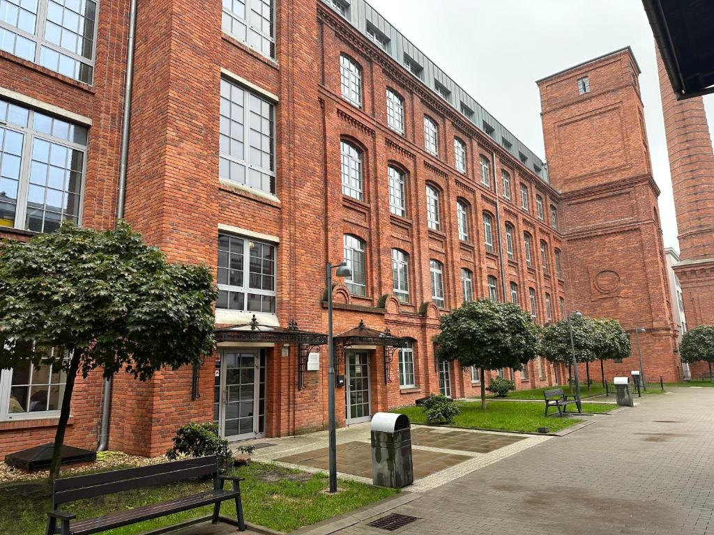een groot bakstenen gebouw met een bank ervoor bij Apartament Szarlotka in Łódź