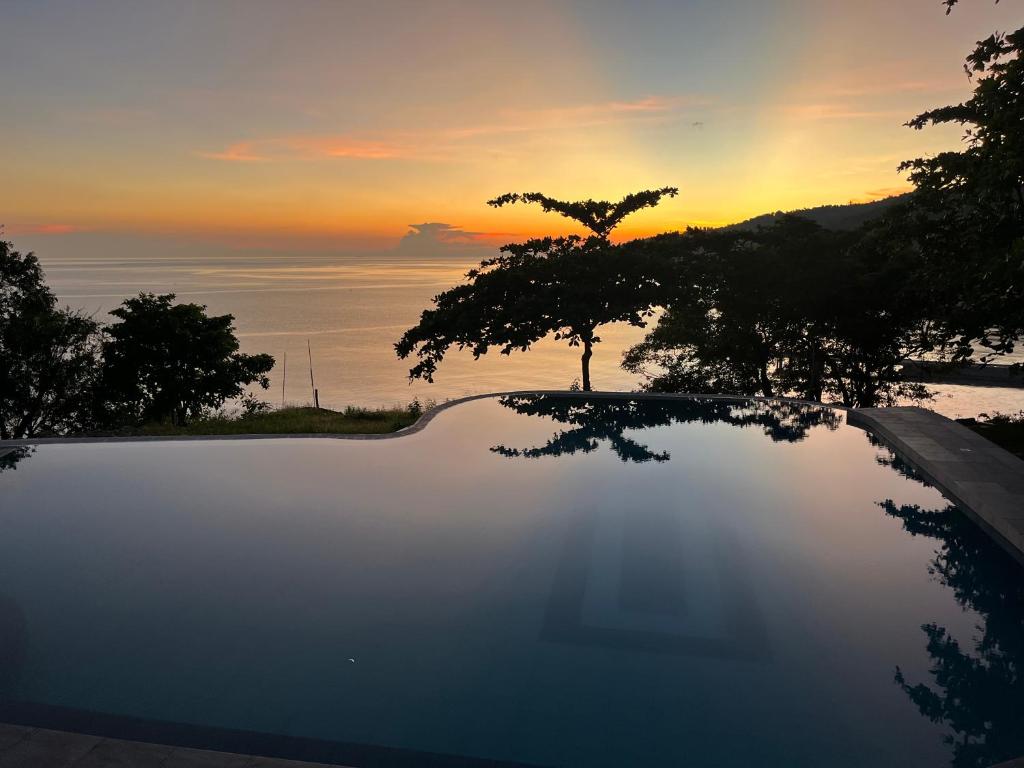 a sunset over a swimming pool with a tree at Virly’z Top View Resort 
