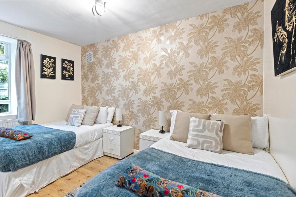 a bedroom with two beds and a wall with palm wallpaper at 3 Bedroom Flat Near Finsbury Park, Manor House Station in London