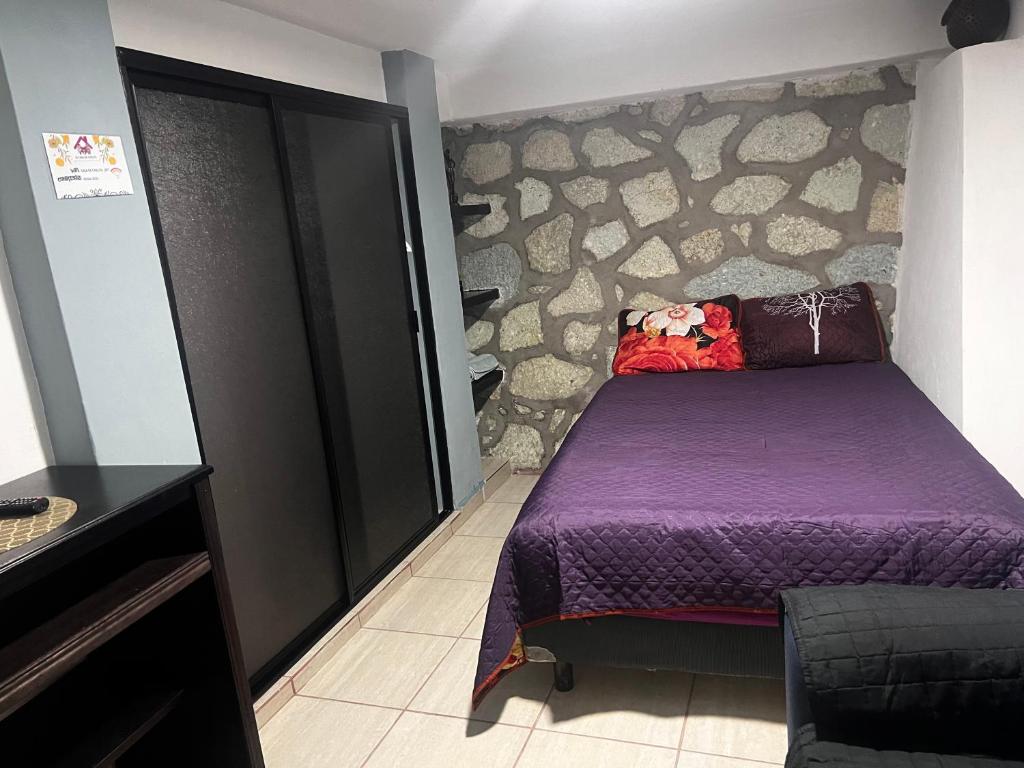 1 dormitorio con cama morada y pared de piedra en Departamento de Cantera en Oaxaca de Juárez