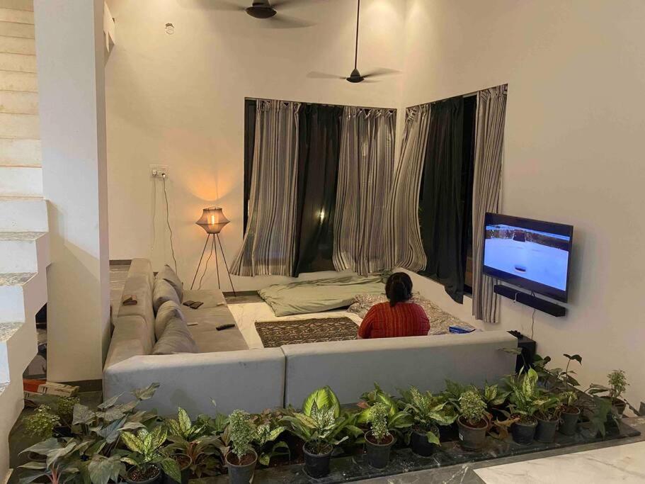 a person sitting on a couch watching a tv in a living room at Palm 3Bhk Villa Alibaug in Alībāg