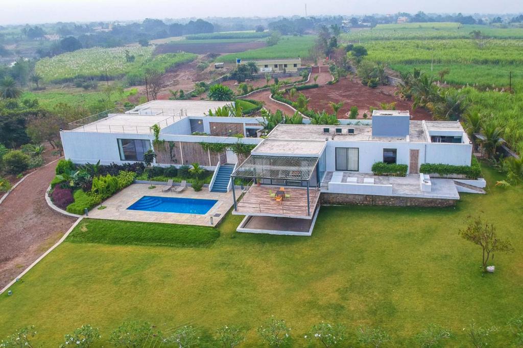 una vista aérea de una casa con un gran patio en Open House by StayVista - Nestled in nature, featuring a Swimming pool & Expansive lawn for a serene retreat, en Shikrapur