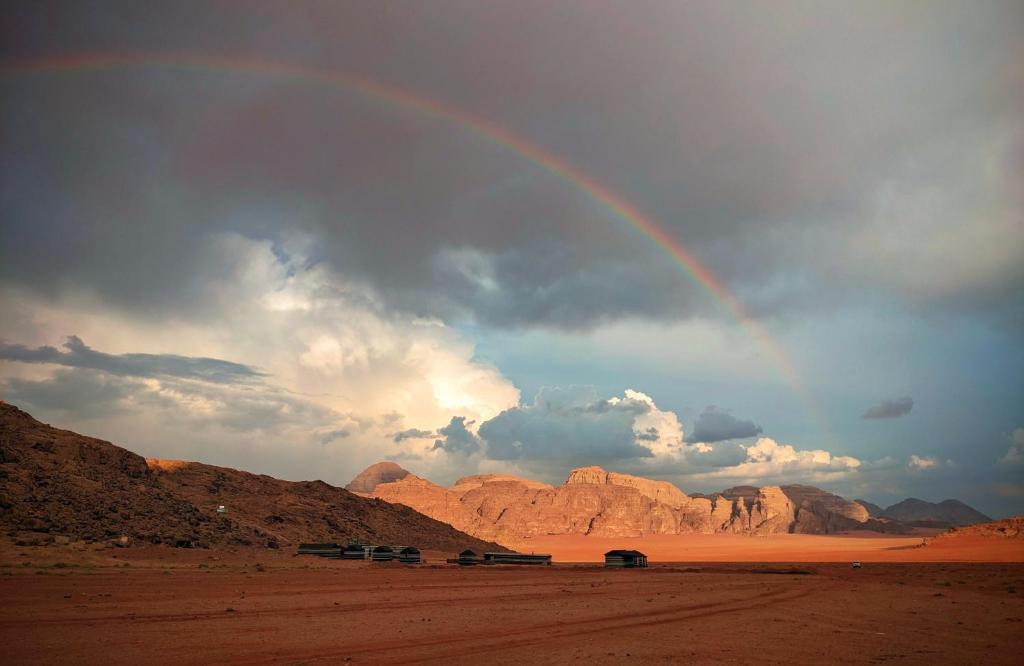 a rainbow in the middle of a desert with cars at Wadi Rum Camp & Jeep Tour in Wadi Rum