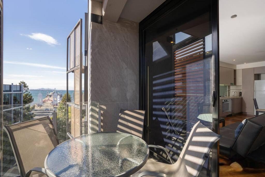 y balcón con mesa de cristal y sillas. en Beachfront Bliss: Luxury Living en Geelong