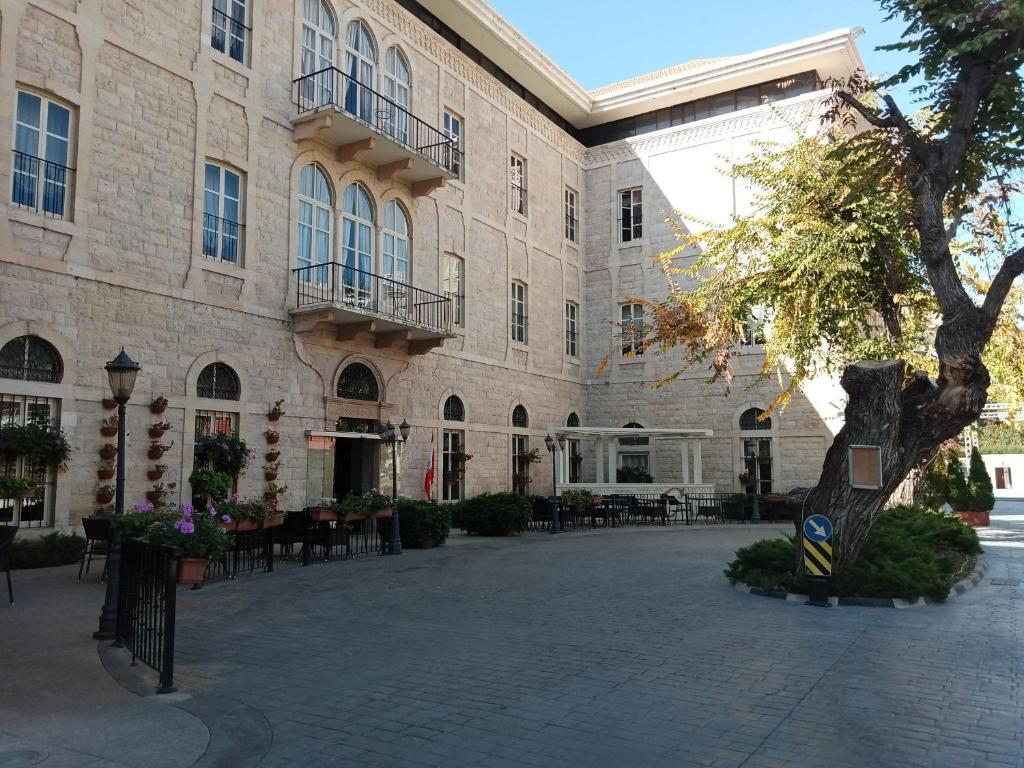 Grand Kadri Hotel - History Marked by Cristal Lebanon في زحلة: مبنى كبير مع ساحة مع طاولات وكراسي