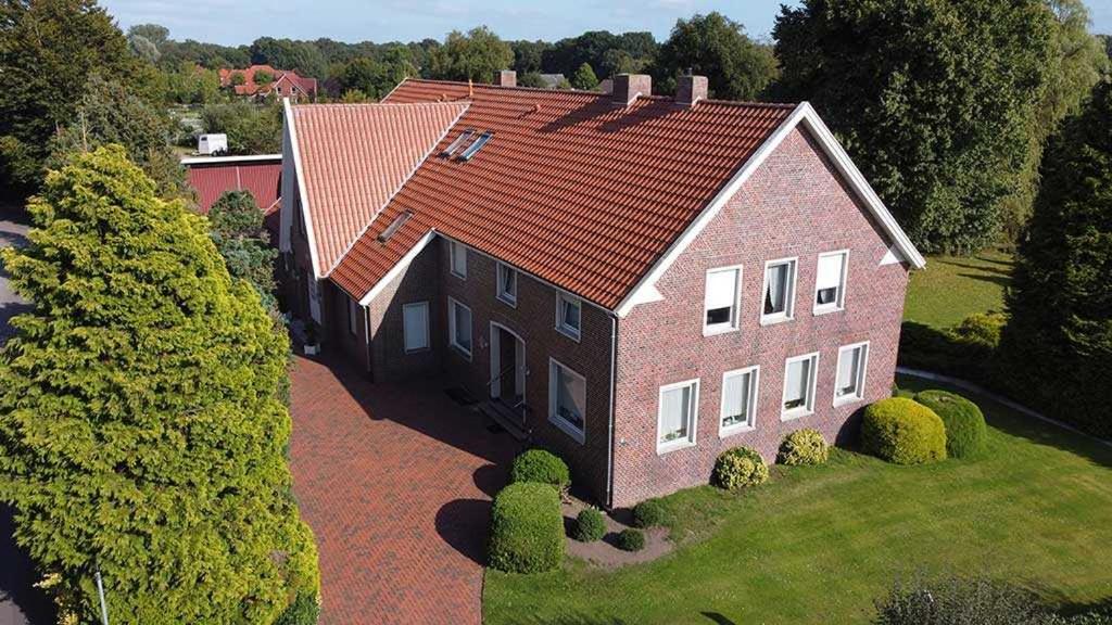 une grande maison en briques avec un toit rouge dans l'établissement Ferienwohnungen Meyerhof_ 55116, à Filsum