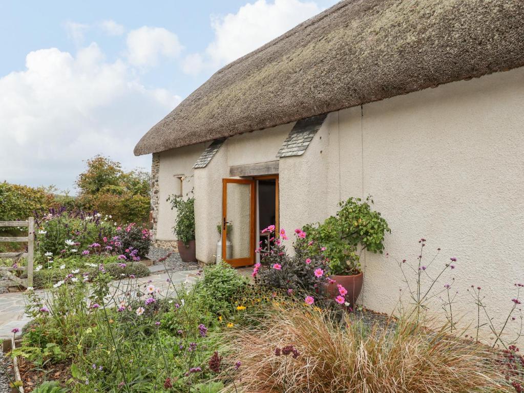 a cottage with a thatched roof and flowers at The Acorn Barn in Exeter