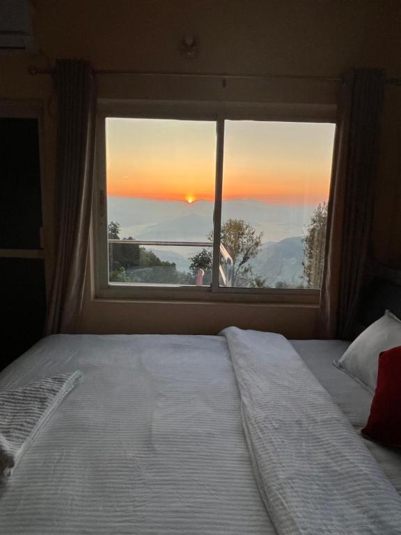 - une chambre avec un lit et une fenêtre donnant sur le coucher du soleil dans l'établissement Hotel Village View Nagarkot, à Nagarkot