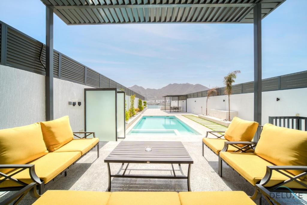 a patio with yellow furniture and a swimming pool at Luxury 4BR Villa with Assistant’s Room Al Dana Island, Fujairah by Deluxe Holiday Homes in Fujairah