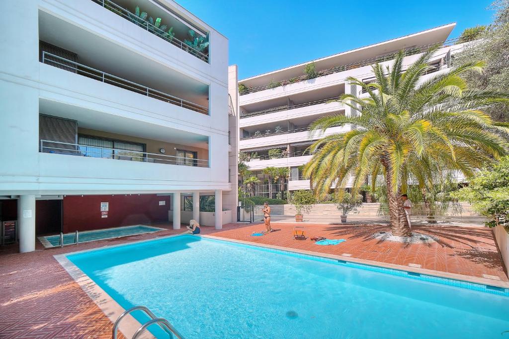 a swimming pool in front of a building with a palm tree at Appartement , piscine, terrasse, proche croisette in Cannes