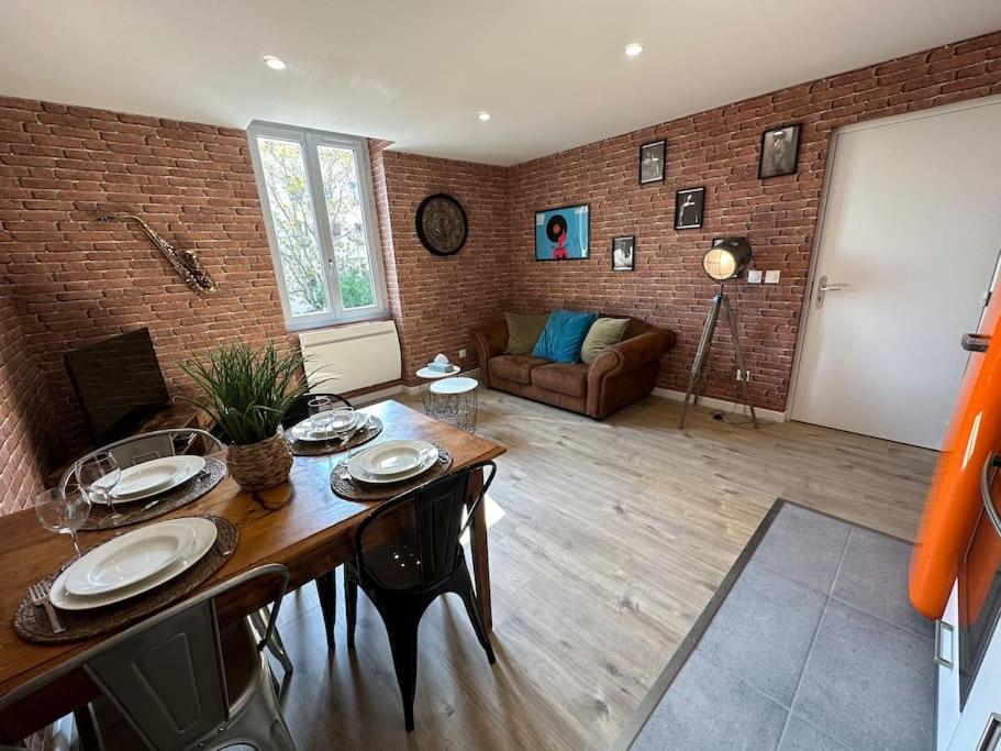 a living room with a table and a brick wall at Appartement JAZZ Vienne nord in Vienne