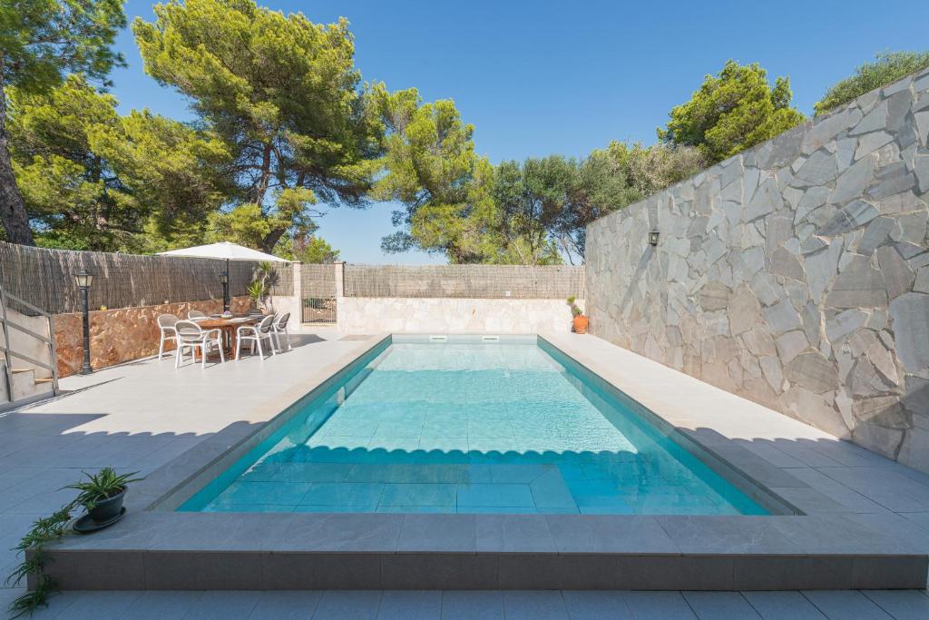 a swimming pool with a table and a stone wall at Garonda Villa in Cala Pi