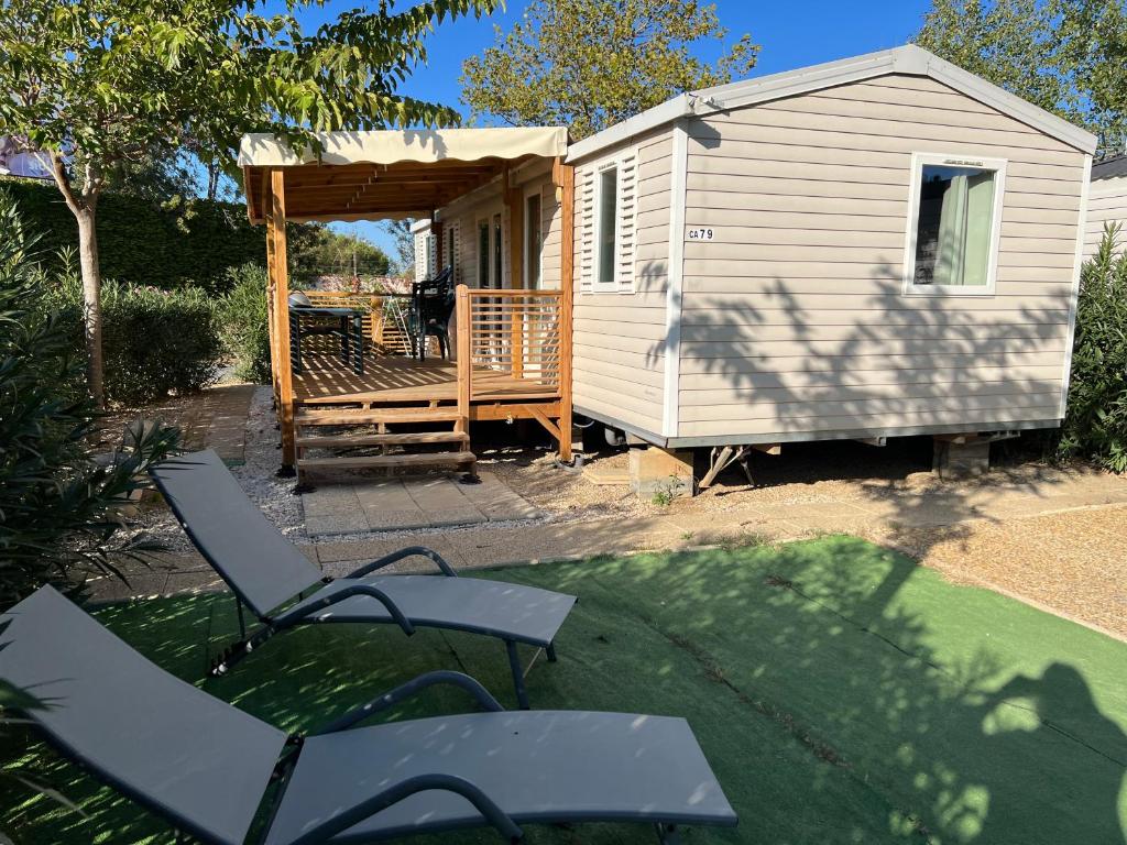 a tiny house with a porch and two chairs at Mobilhome La Carabasse Vias Plage in Vias