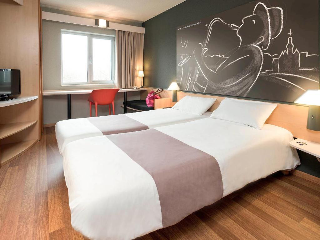 a hotel room with a large bed and a painting on the wall at ibis Dinant Centre in Dinant