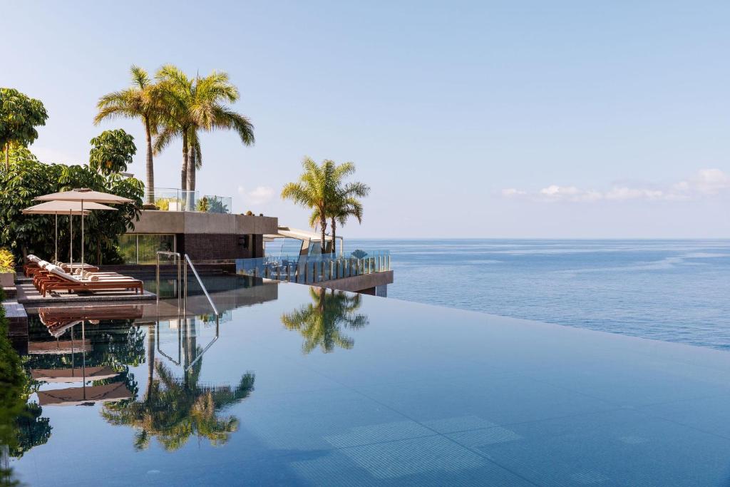 a swimming pool next to the ocean with palm trees at Saccharum - Resort and Spa - Savoy Signature in Calheta