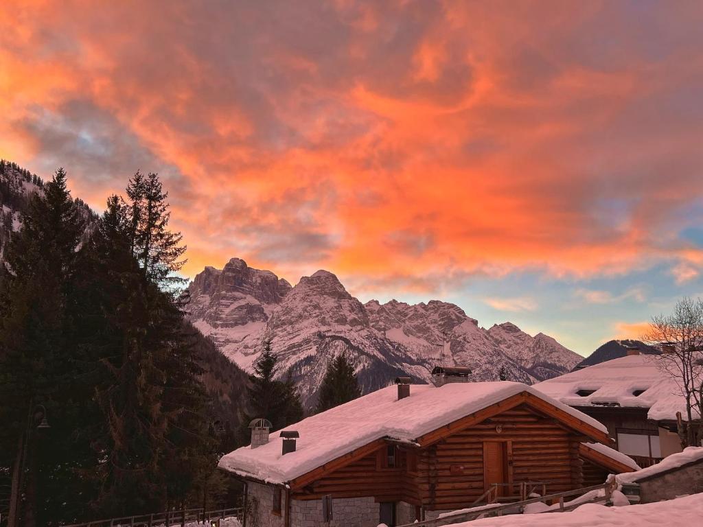 a cabin with a snow covered roof in front of mountains at Bonapace Dolomites Apartments in Madonna di Campiglio
