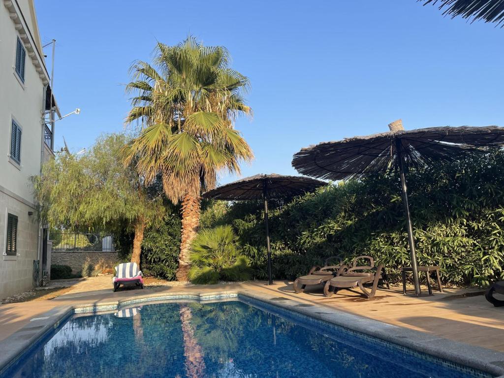 a swimming pool with two umbrellas and two chairs at 2 Bed Flat - Sleeps 6 - Pool - Garden - Parking in Milna