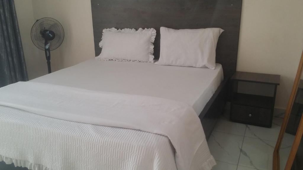 - un lit avec des draps et des oreillers blancs dans l'établissement PagersHome Suites - Classic Nyarutarama, à Kigali