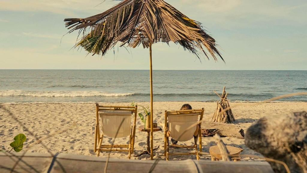 Dos sillas y una sombrilla en la playa en Lote 10 Glamping, en Guachaca
