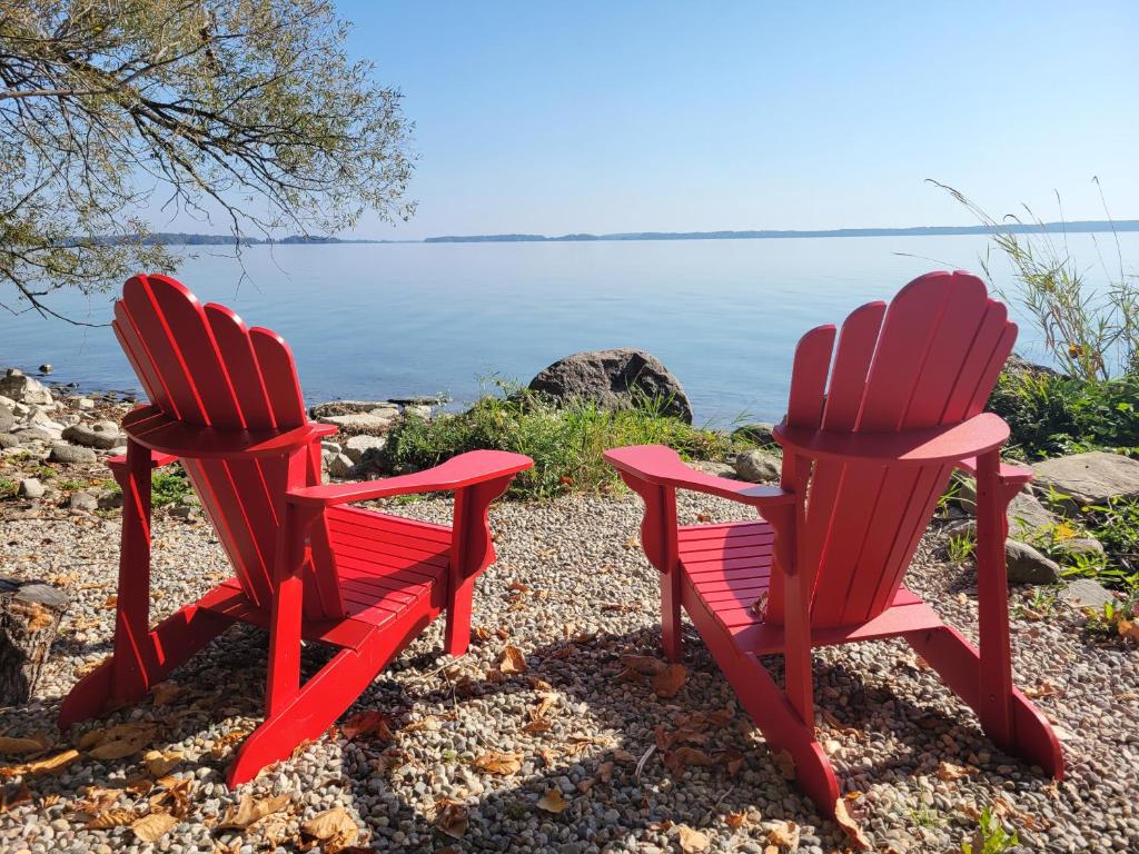 two red chairs sitting next to the water at Unique waterfront house with private beach in Gananoque