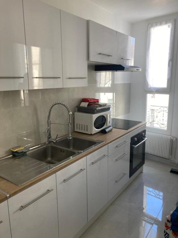 Una cocina con gabinetes blancos, un fregadero y un microondas. en mon appartement en centre ville, en Le Pré-Saint-Gervais