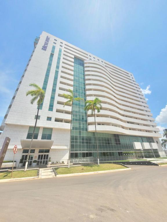 a tall building with palm trees in front of it at Brasília By Rei dos Flats in Brasília