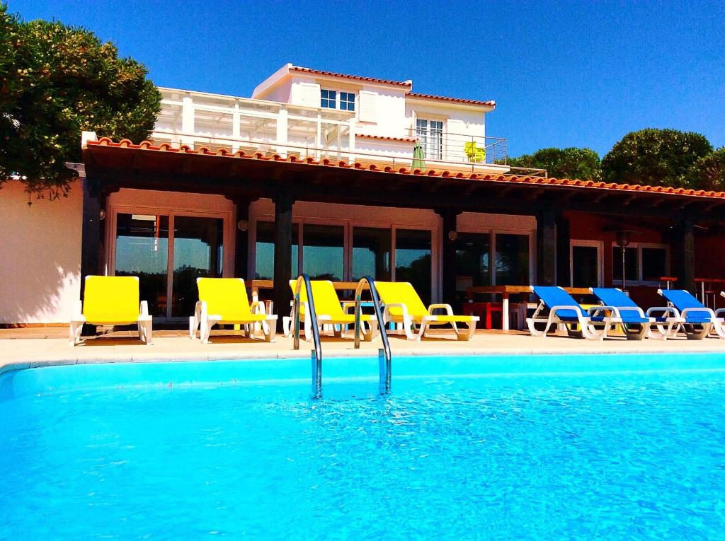 a pool with yellow and blue chairs and a house at FreeSurfCamp & Hostel in Peniche