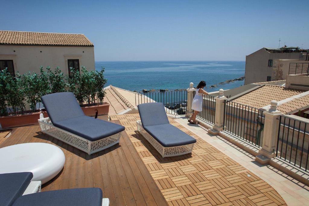 a woman standing on a deck with chairs and the ocean at Algilà Ortigia Charme Hotel in Siracusa