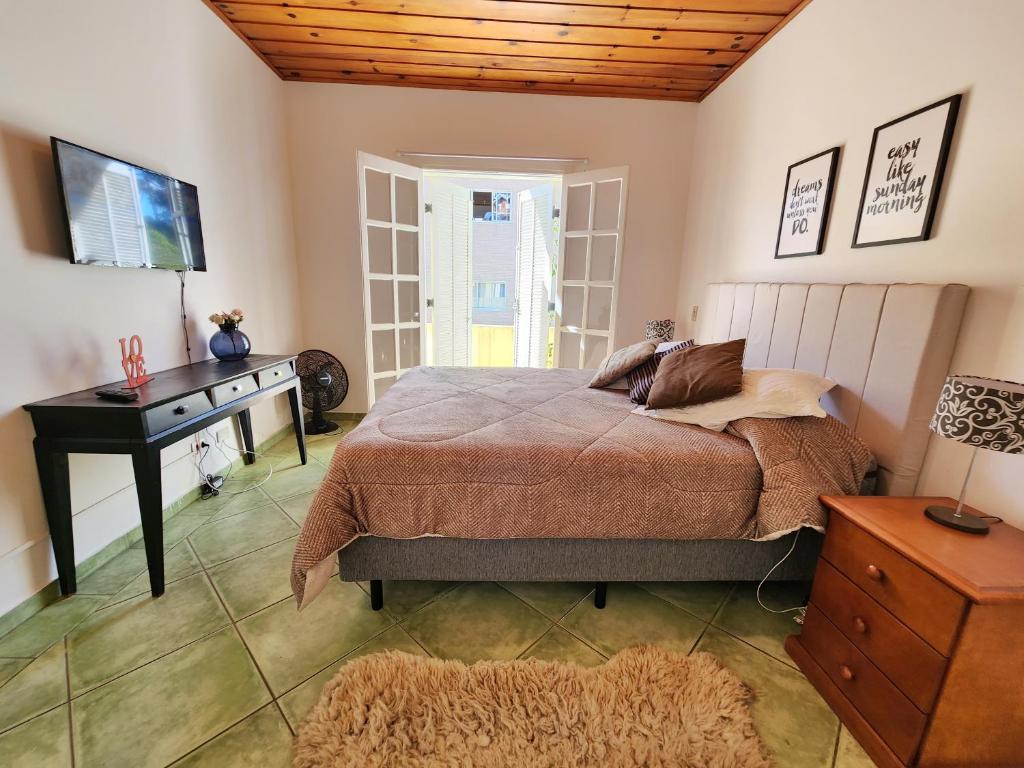 Dormitorio con cama, escritorio y TV en Quatro Estacoes Hospeda -Vila 01 , sua casa em Campos do Jordao, a 1 km do centro turistico, en Campos do Jordão