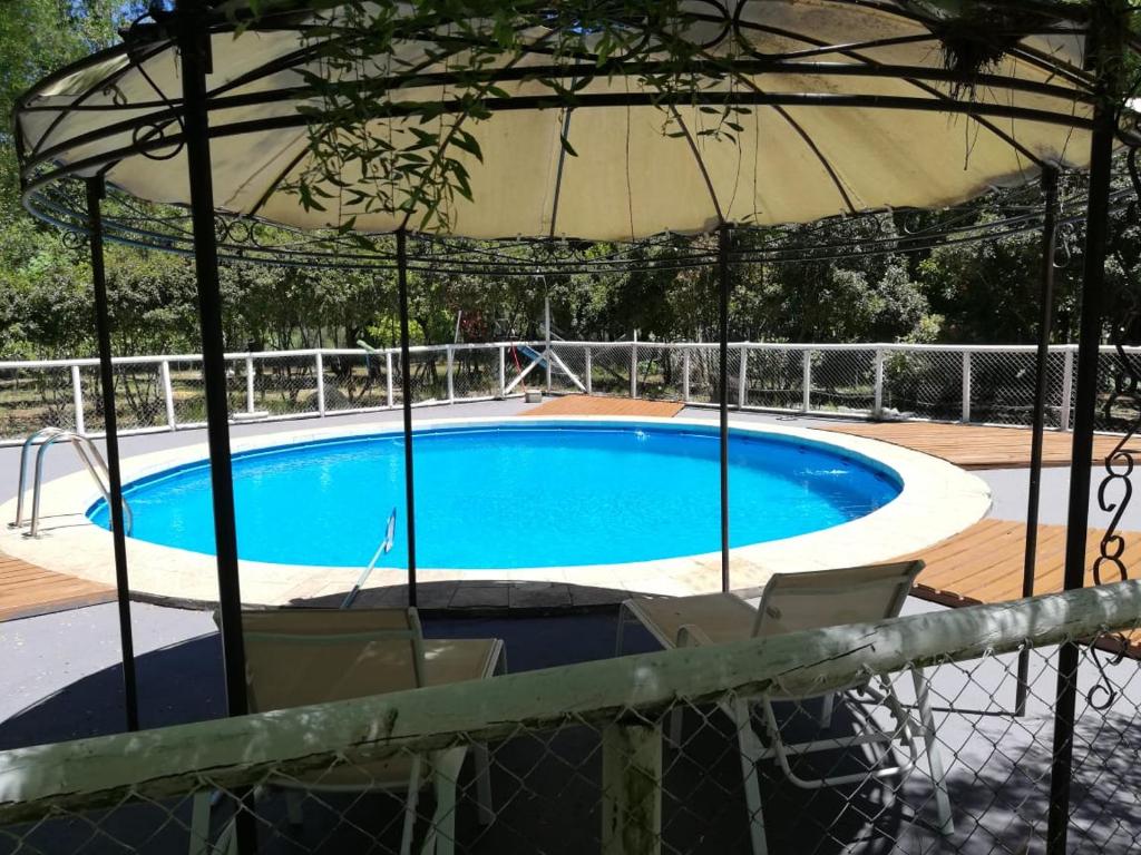 uma piscina com um guarda-sol e duas cadeiras em Cabaña Paso De Los Toros, San Fabian de Alico em San Fabián de Alico