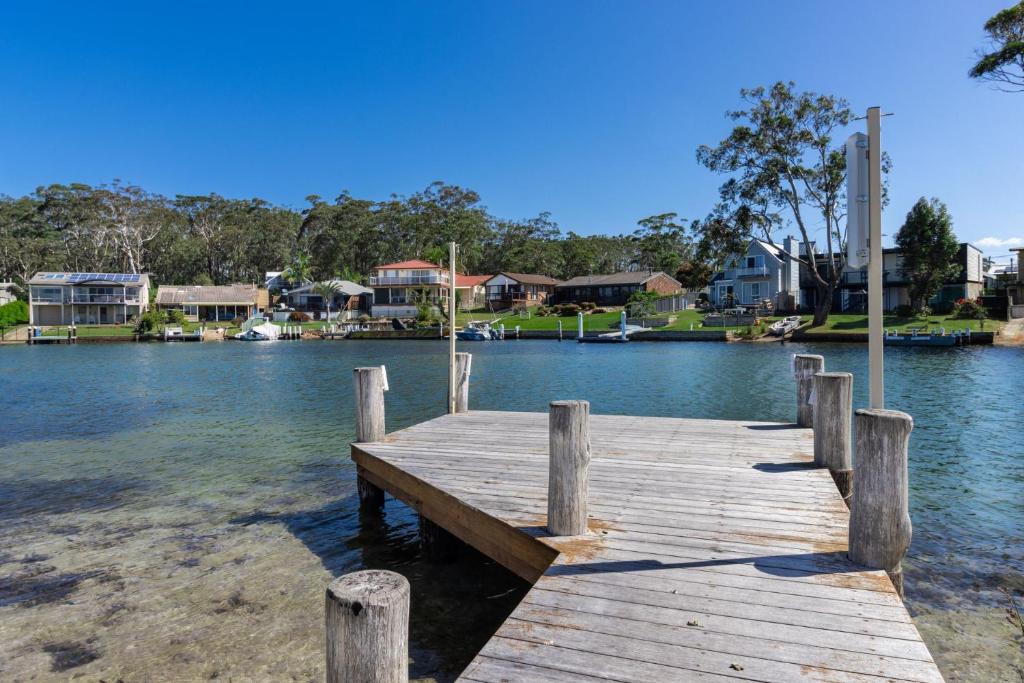 a wooden dock in the water with houses in the background at Cormorant Waterfront Home in Sussex Inlet