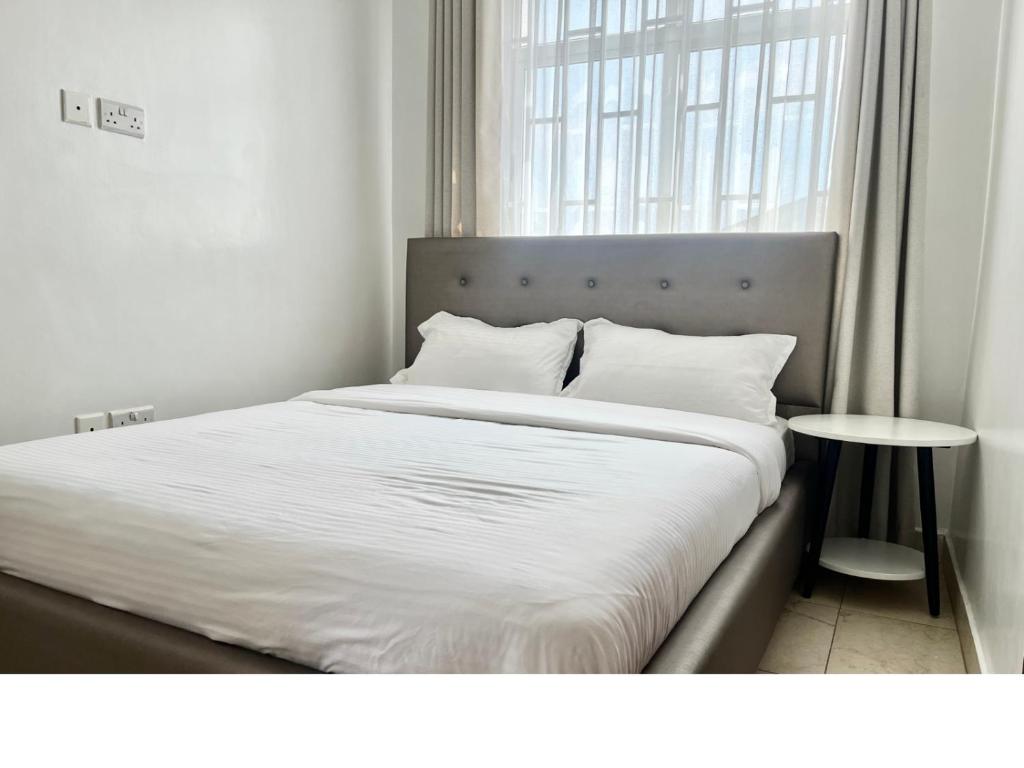 a bed with white sheets and pillows next to a window at Neema Suites, Ngong RD near Junction in Nairobi