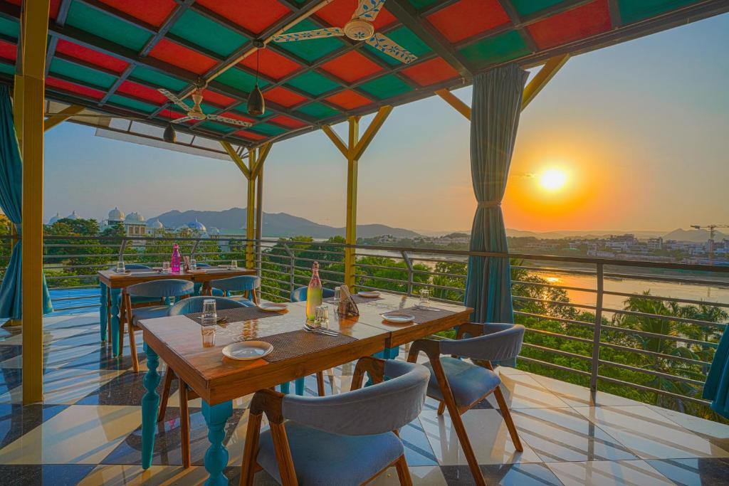 ein Restaurant mit Tischen und Stühlen auf einem Balkon mit Blick auf den Sonnenuntergang in der Unterkunft AAJ HAVELI - Lake Facing Boutique Hotel by Levelup Hotels in Udaipur