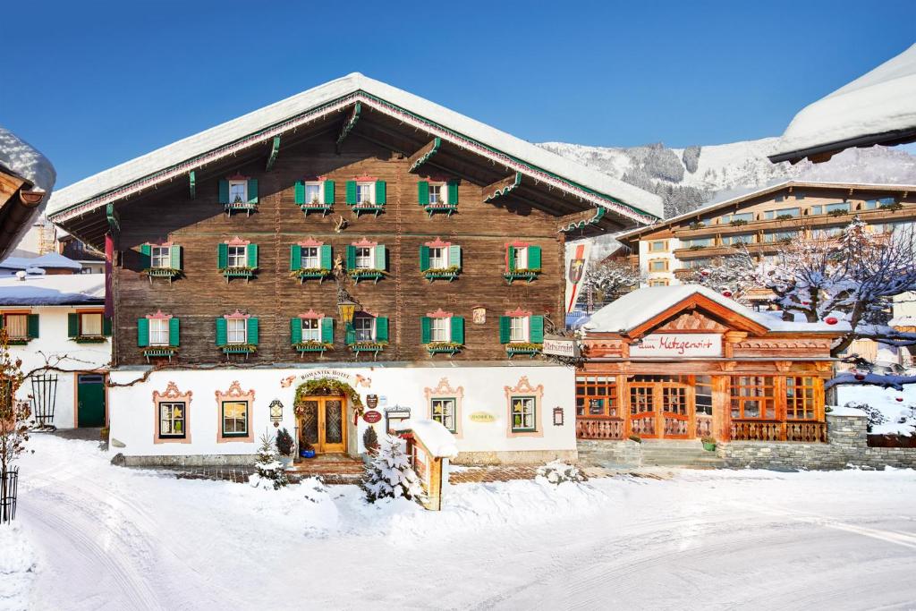 a large wooden building with green shuttered windows in the snow at Romantikhotel Zell am See in Zell am See