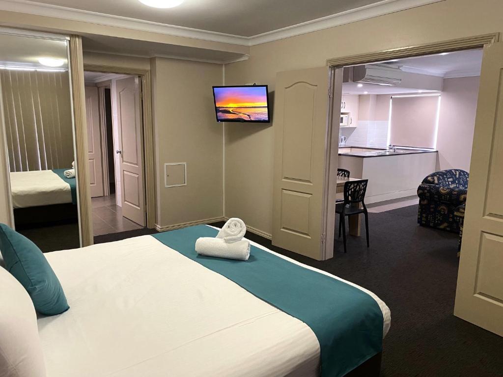 Habitación de hotel con cama y TV en la pared en City Ville Apartments and Motel, en Rockhampton