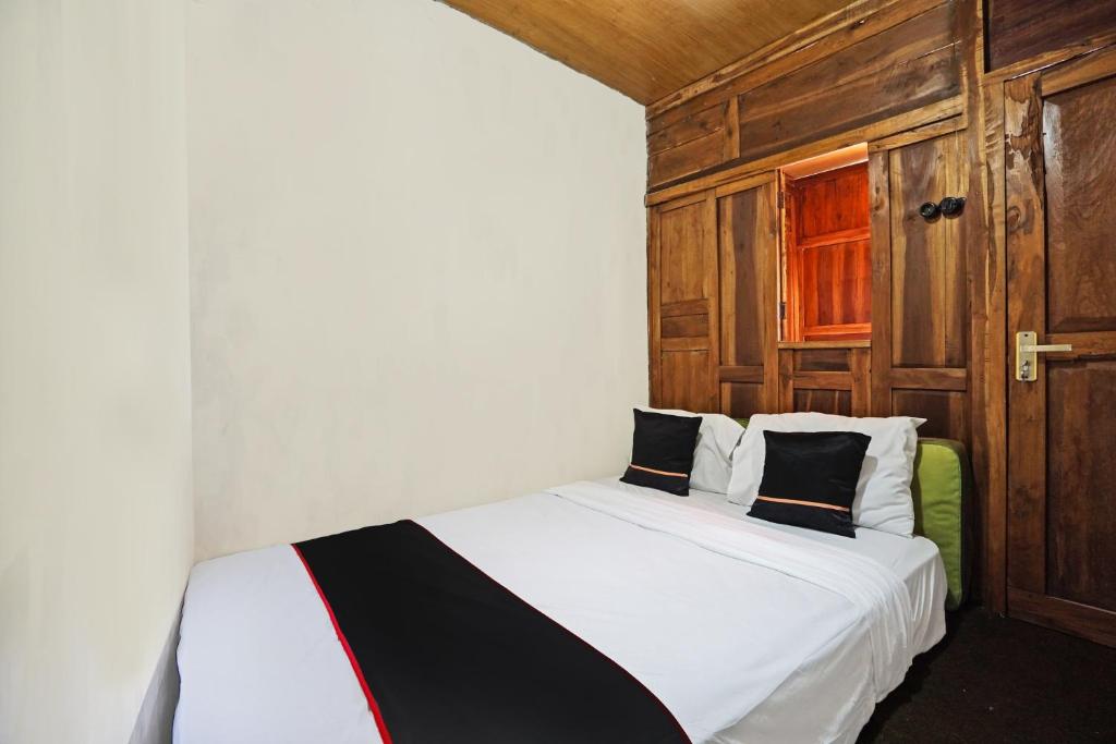 1 dormitorio con cama blanca y almohadas blancas y negras en Lembah Mbalong Resort Mitra RedDoorz Near Exit Tol Singosari en Blimbing