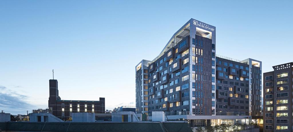 a tall glass building in a city at Noblepia Hotel in Seogwipo