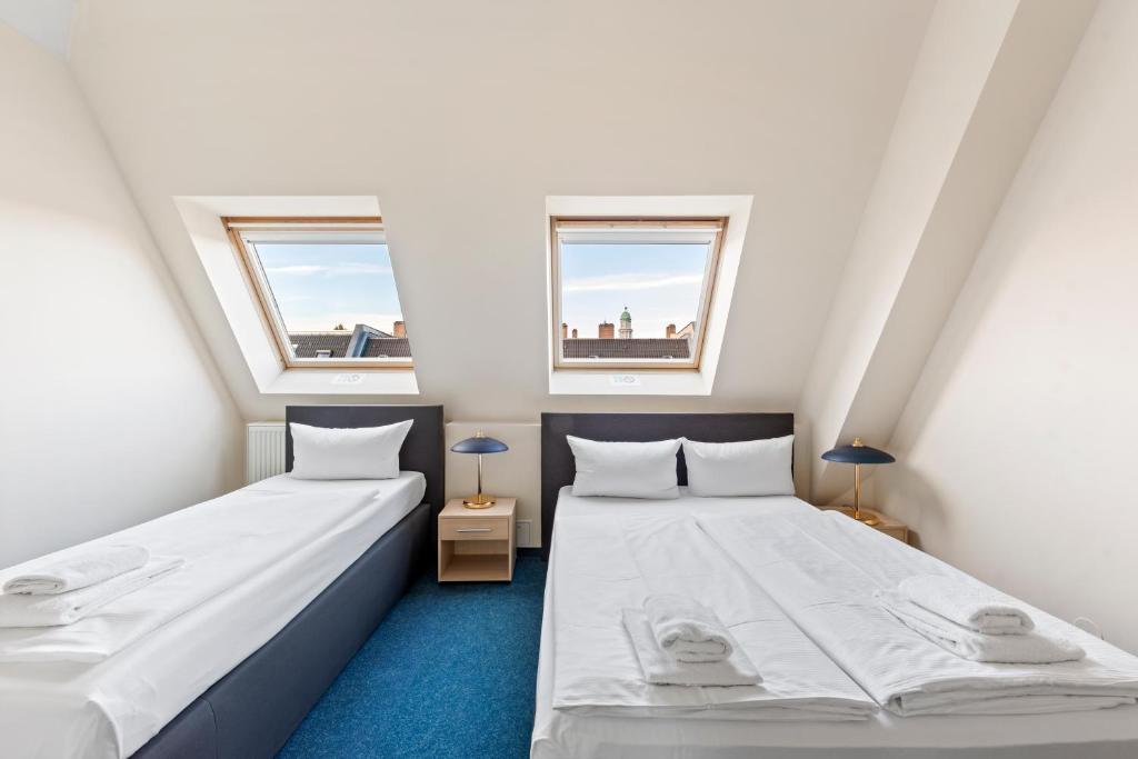 two beds in a small room with two windows at Hotel Comenius in Berlin